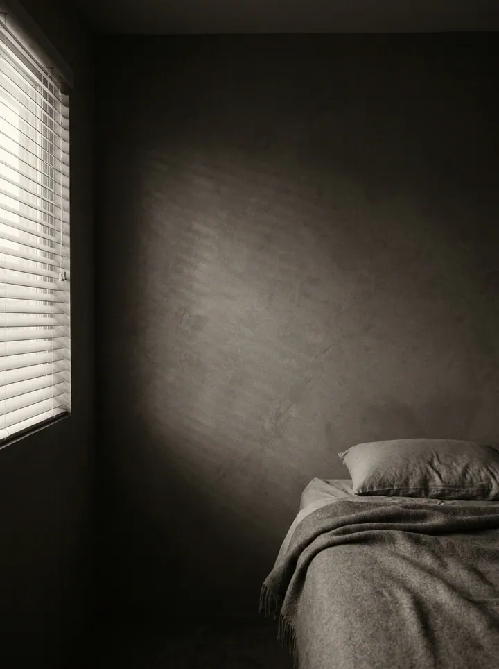 Soft morning light through blinds onto a bedroom wall.