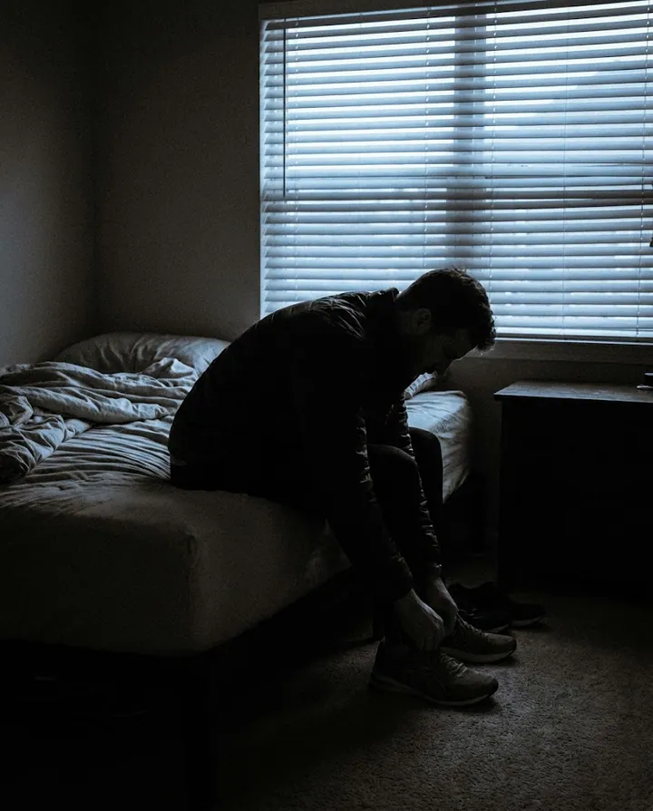 Silhouette of a man tying running shoes on the edge of a bed at 5:15 a.m.